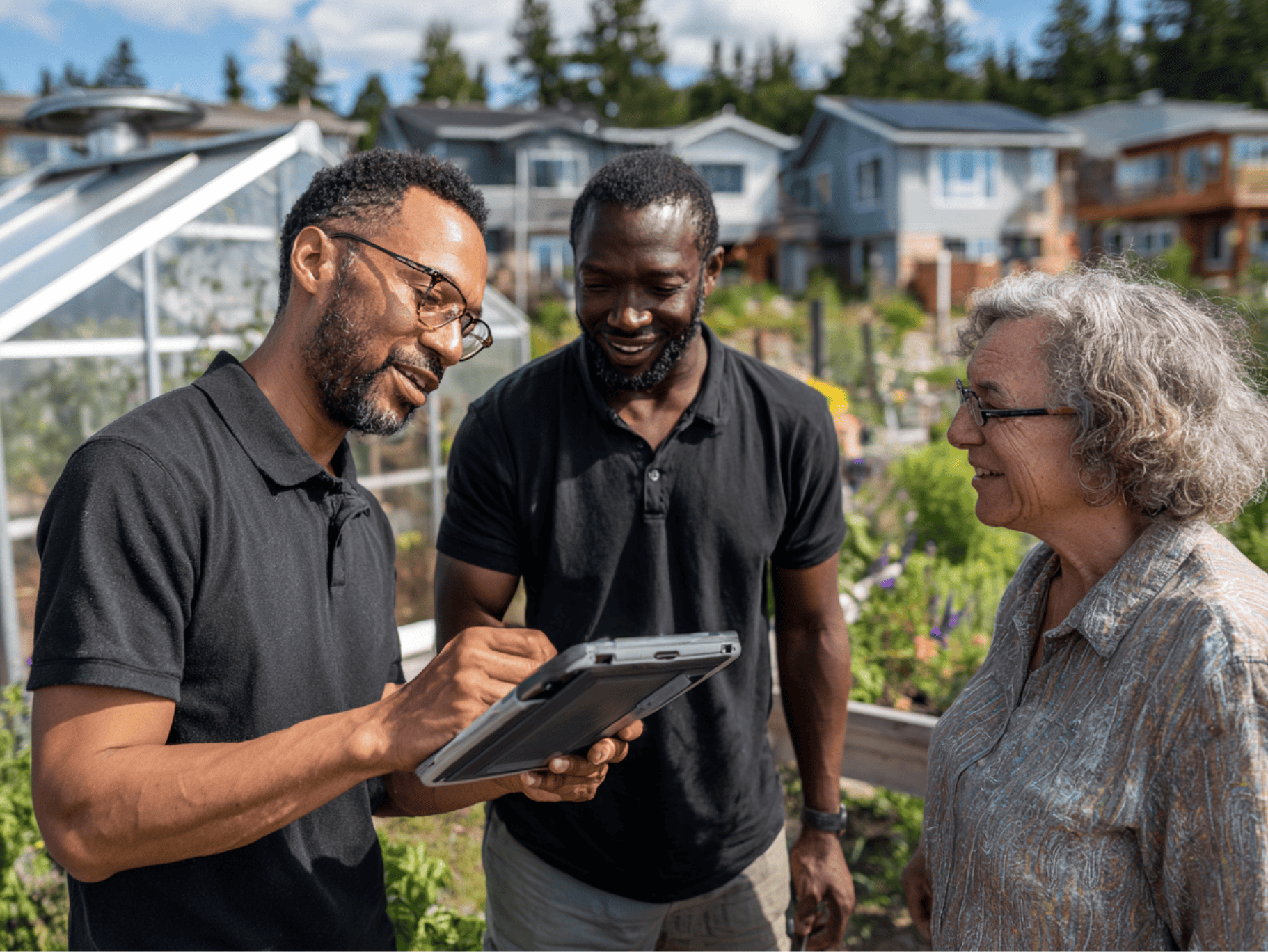 Two thermal energy auditors speaking with a community member in front of a community greenhouse